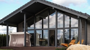 Une maison moderne avec de grandes fenêtres, un patio couvert et une pierre au premier plan.