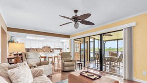 A spacious living area with a sofa, ottoman, and chairs, a ceiling fan, and a view to an outdoor patio. - Sea Club #29 - Our Sunrise Nest (Indian Shores)