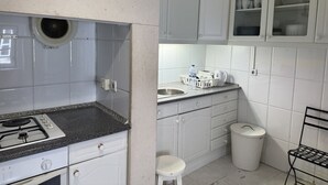 A compact kitchen with white cabinets, a gas stove, a sink, and a trash bin. - Rossio Terrace (Lisbon)