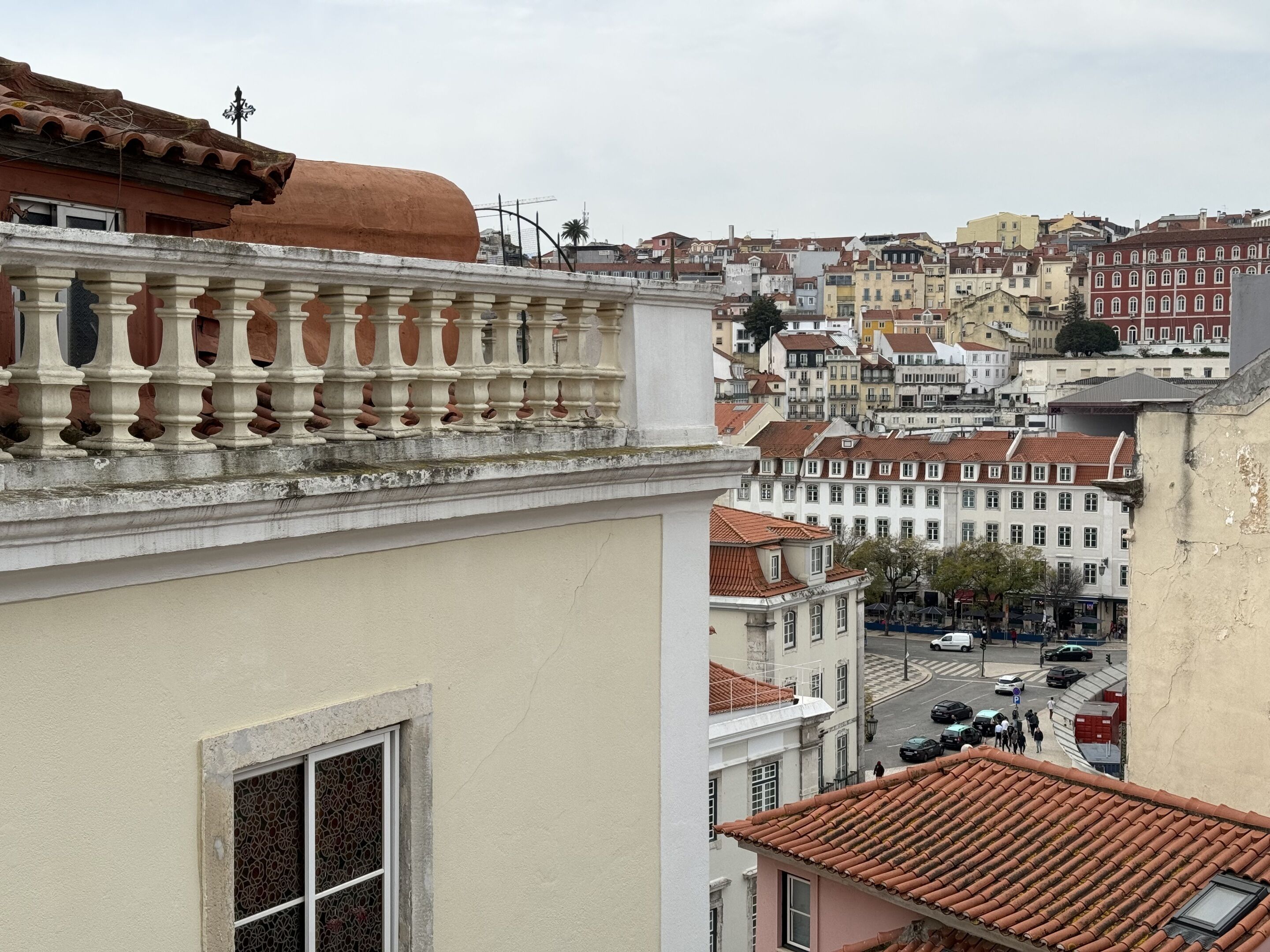 A view of a cityscape with buildings featuring red-tiled roofs and a prominent balcony with a balustrade.
