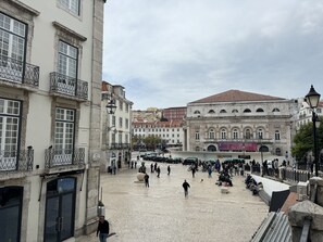 A historic square with cobblestone pavement, surrounded by classical buildings with ornate balconies and large windows. - Rossio Terrace (Lisbon)