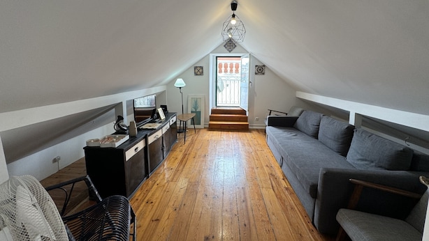 A cozy attic bedroom with a wooden floor, a gray sofa, a desk with a computer, and a staircase leading to a balcony. - Rossio Terrace (Lisbon)