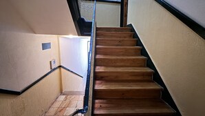 A wooden staircase with a metal handrail, leading to a landing with a white wall and a small window. - Rossio Terrace (Lisbon)