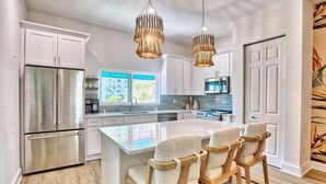 Una cocina moderna con electrodomésticos de acero inoxidable, una isla central con taburetes de bar e iluminación colgante.