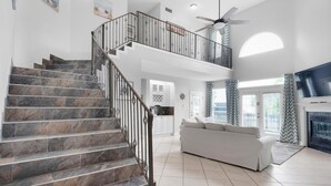 A spacious living area with a marble staircase, a white sofa, and a fireplace. - Serenity by the Sea (Destin)