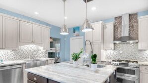 A modern kitchen with white cabinets, a marble island, stainless steel appliances, and pendant lighting. - Serenity by the Sea (Destin)