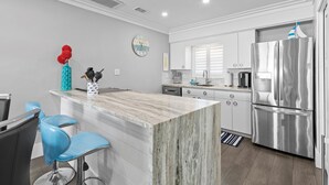 Een moderne keuken met een marmeren eiland, roestvrijstalen apparatuur en blauwe barkrukken.