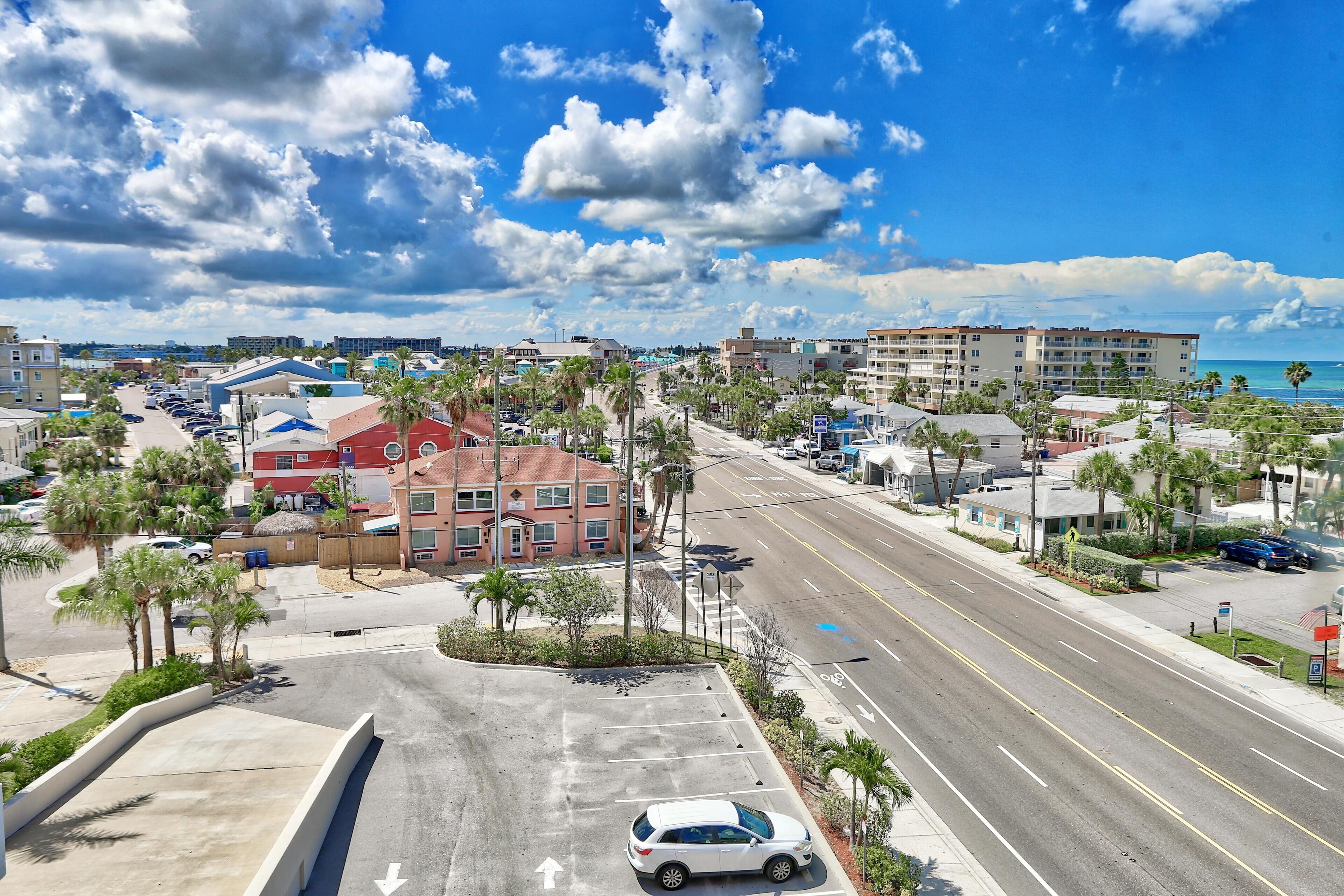 A coastal urban street with a parking lot, buildings, and a clear view of the ocean.