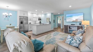 A modern living room with a beige sofa, a coffee table, and a TV mounted on the wall. - Coronado Arms Condominiums B-18 (New Smyrna Beach)