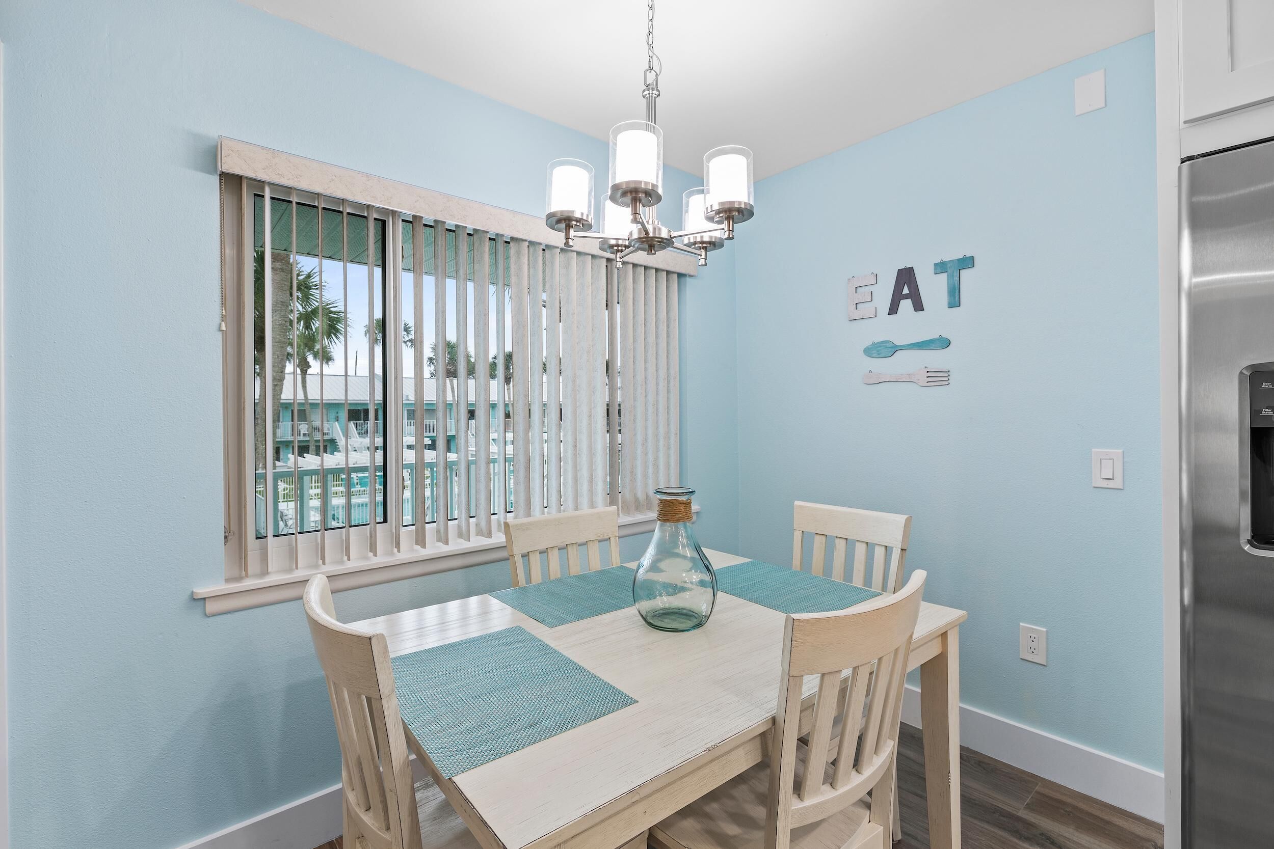 A dining area with a table, chairs, a chandelier, and a wall with a 'GREAT' sign.
