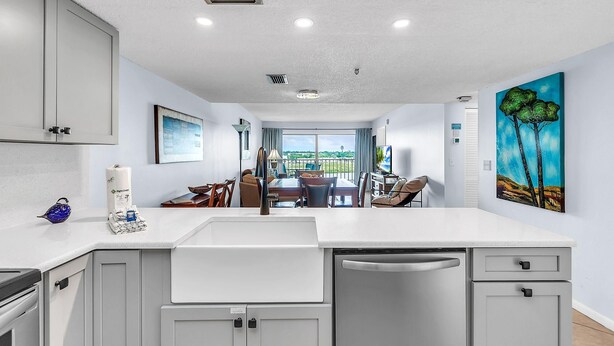 A modern kitchen with white cabinetry, a central island, and a view to the dining area. - Sea Club #503 - Coastal Breeze (Indian Shores)