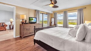 A hotel room with a bed, a television, a ceiling fan, and large windows with curtains. - Sea Club #503 - Coastal Breeze (Indian Shores)