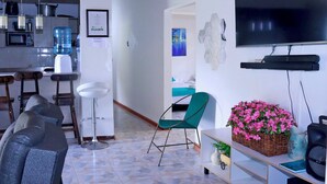 Una sala moderna con un sofá, un sillón verde, un televisor y una cocina con dispensador de agua.