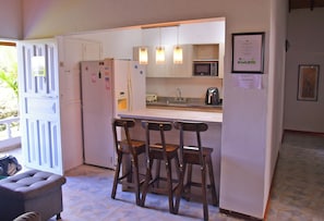 Cozinha compacta com geladeira, micro-ondas e banquetas de bar.
