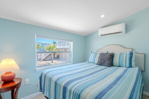A bedroom with a bed, a window, a lamp, and an air conditioner. - Island Paradise Cottage (Fort Myers Beach)