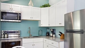 A modern kitchen with white cabinets, a stainless steel refrigerator, a built-in microwave, and a kettle on the stove. - Island Paradise Cottage (Fort Myers Beach)