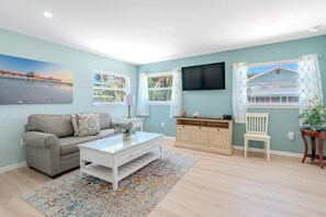 A living room with a sofa, coffee table, TV, and windows with curtains. - Island Paradise Cottage (Fort Myers Beach)