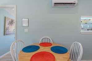 A dining area with a wooden table, four chairs, and a wall-mounted air conditioner. - Island Paradise Cottage (Fort Myers Beach)