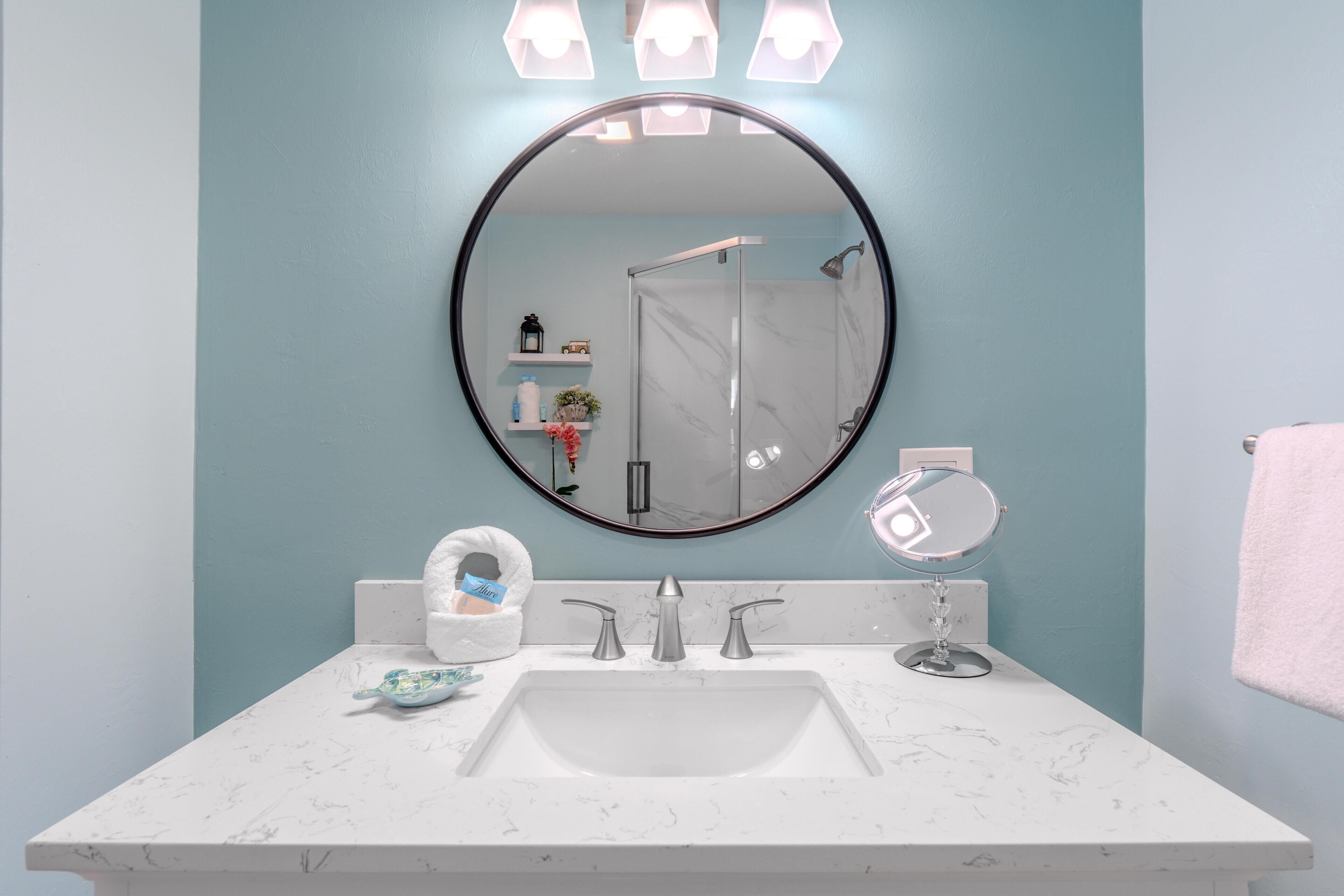 A bathroom with a white marble sink, a round mirror, a handheld mirror, and a towel rack.
