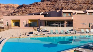 A modern hotel with a pool, lounge chairs, and a mountain backdrop. - Spacious 2-bedroom condo with AC, WiFi in Magical Moab (Moab)