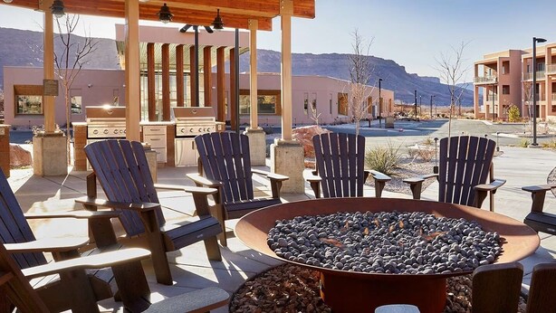 An outdoor seating area with Adirondack chairs and a fire pit, overlooking a parking lot and buildings. - Spacious 2-bedroom condo with AC, WiFi in Magical Moab (Moab)