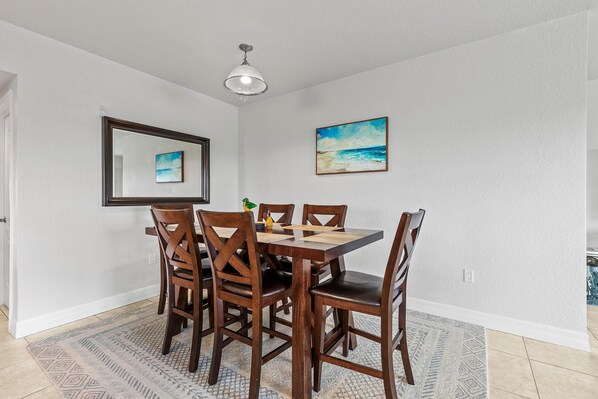 A dining area with a wooden table and chairs, a rug, a ceiling light, and two framed pictures on the wall.