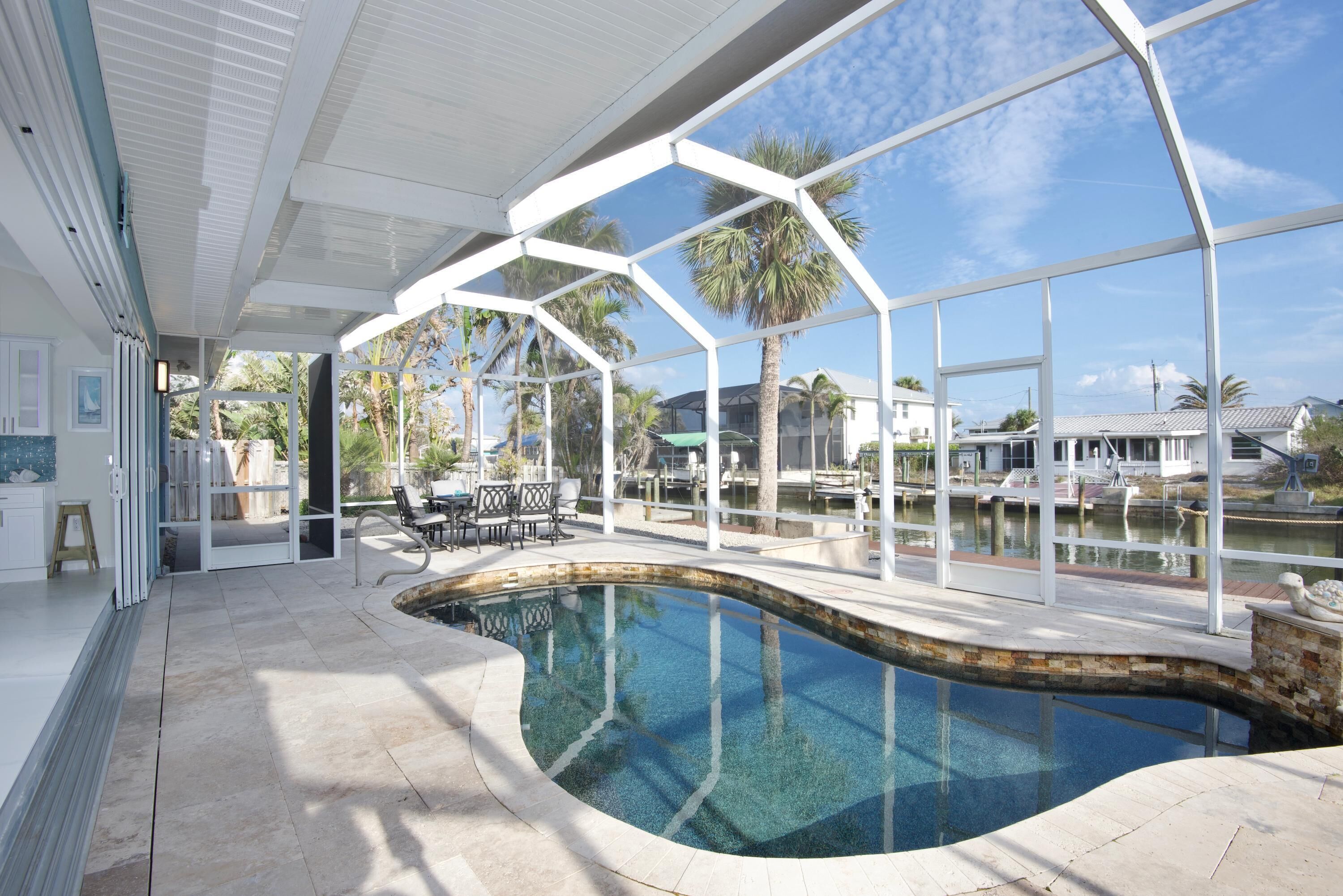 A modern indoor pool area with clear views of the surrounding landscape, including palm trees and a body of water.