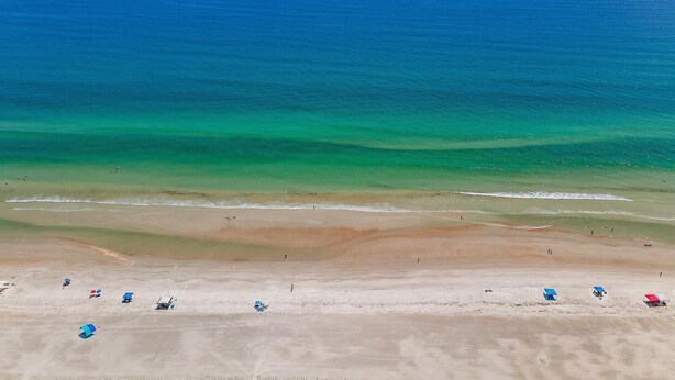 Een strand met helderblauw water, een zandstrand en diverse strandparasols.