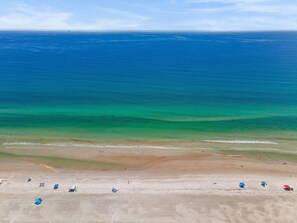 A beach with clear blue water, a sandy shore, and several beach umbrellas.