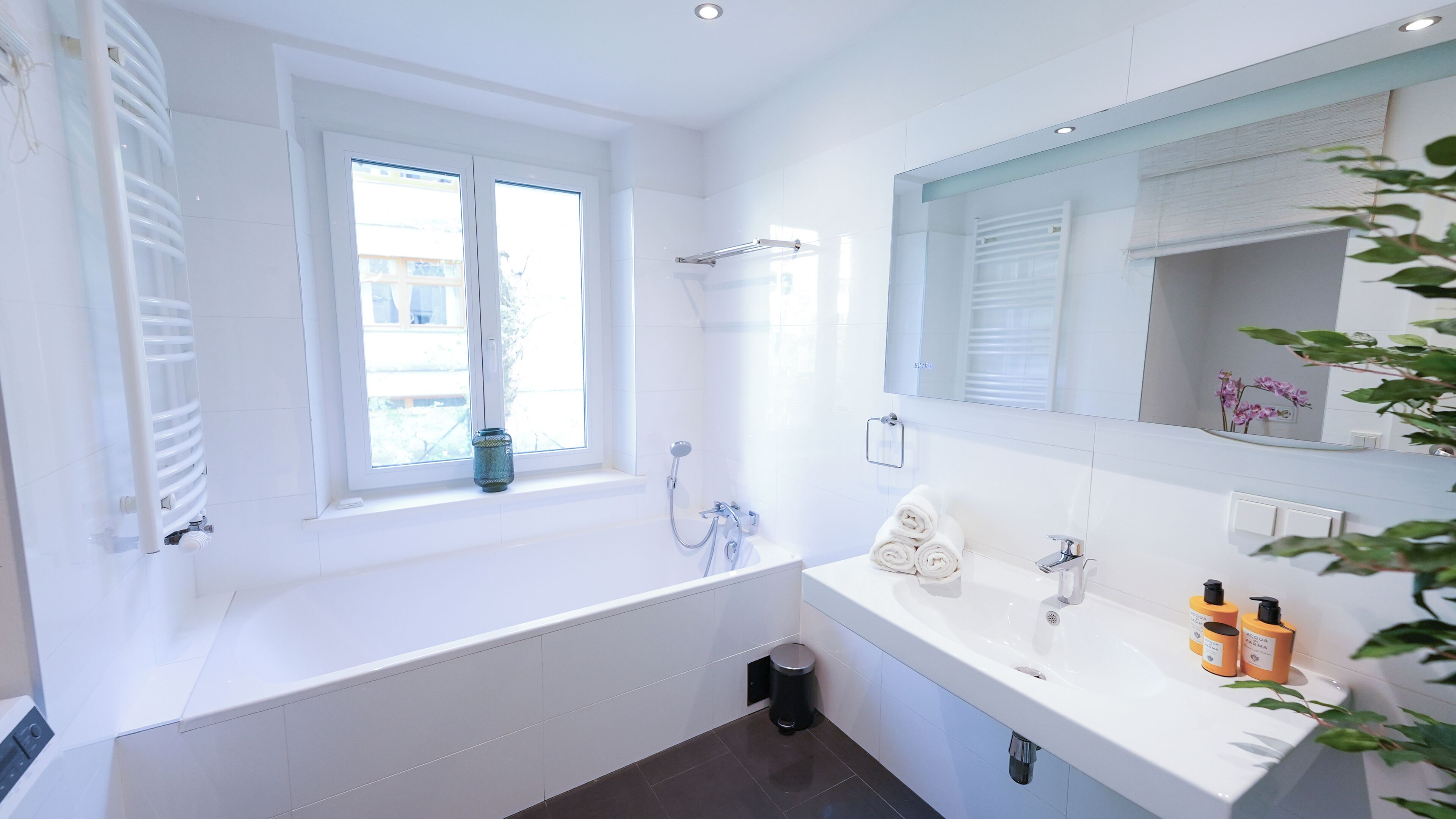 Un baño moderno con bañera, ducha, lavabo con artículos de aseo y ventana con vistas.