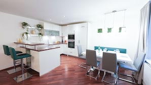 Una cocina moderna con armarios blancos, una isla central con pileta y un comedor con mesa y sillas.