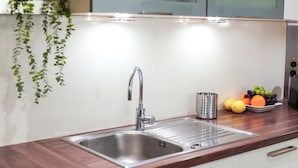 Una cocina con un lavamanos de acero inoxidable, un frutero con naranjas y uvas, y un colador de acero inoxidable.