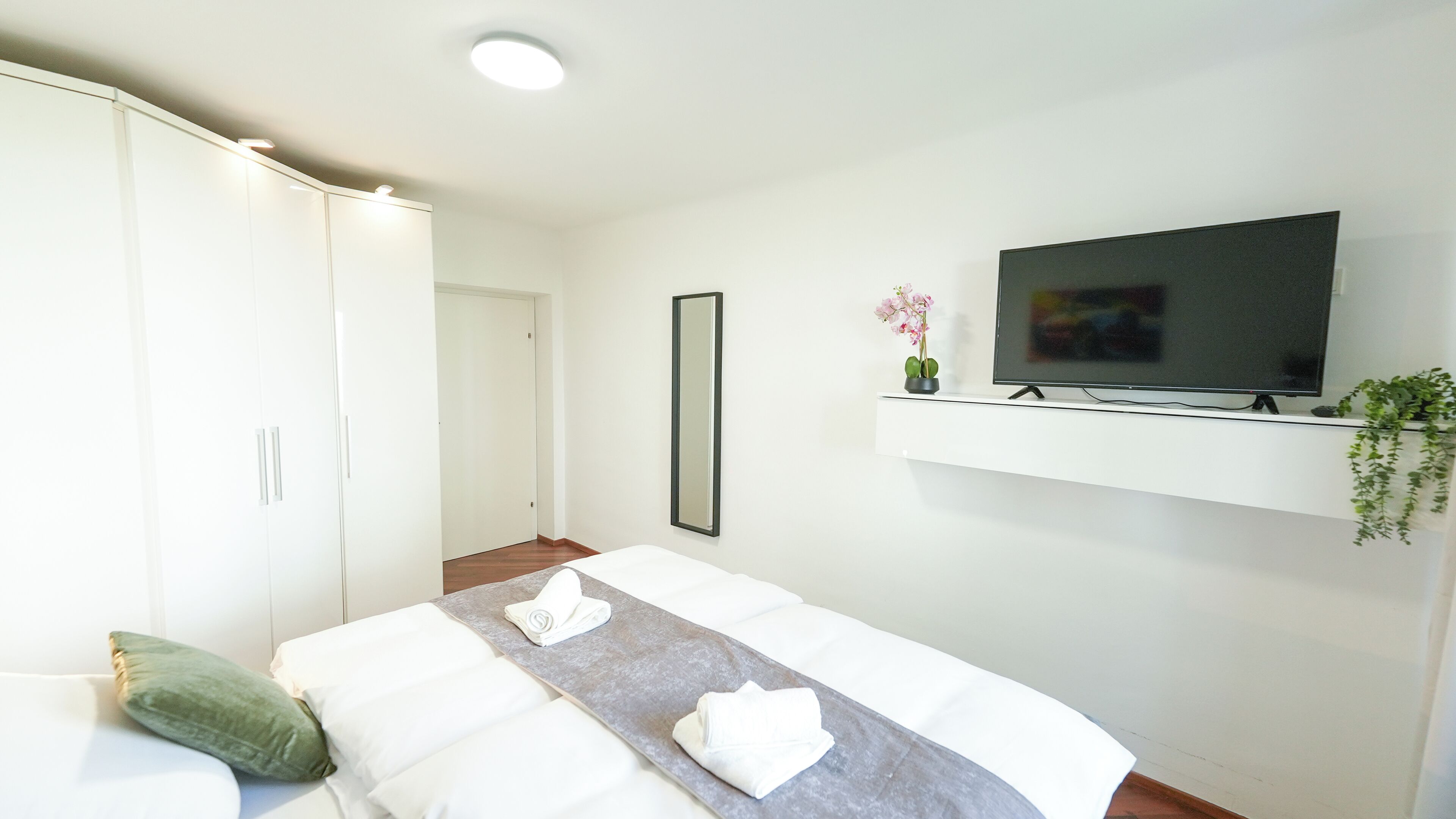 Habitación de hotel con cama, televisor montado en estante, armario y espejo.