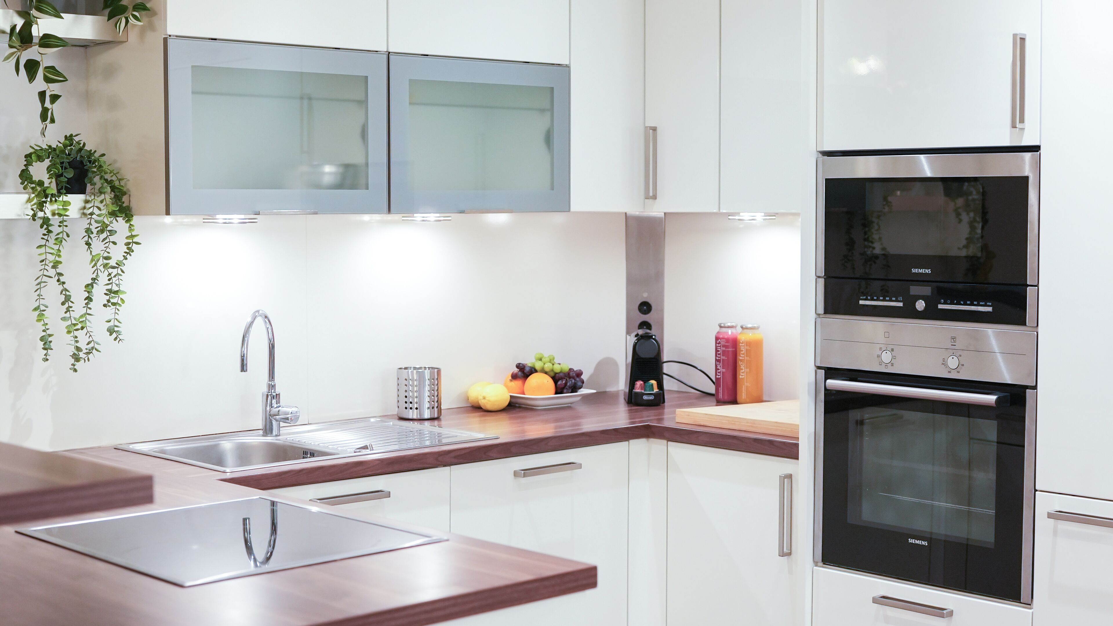 Una cocina moderna con gabinetes blancos, electrodomésticos de acero inoxidable, un lavamanos y un frutero.