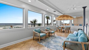 Amplia sala de estar con grandes ventanales que dan a la playa, mobiliario de mimbre y un tapete con motivos tropicales.
