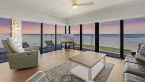 Ein modernes Wohnzimmer mit Blick auf den Strand, einem Deckenventilator und einem Fernseher auf einem Standfuß.