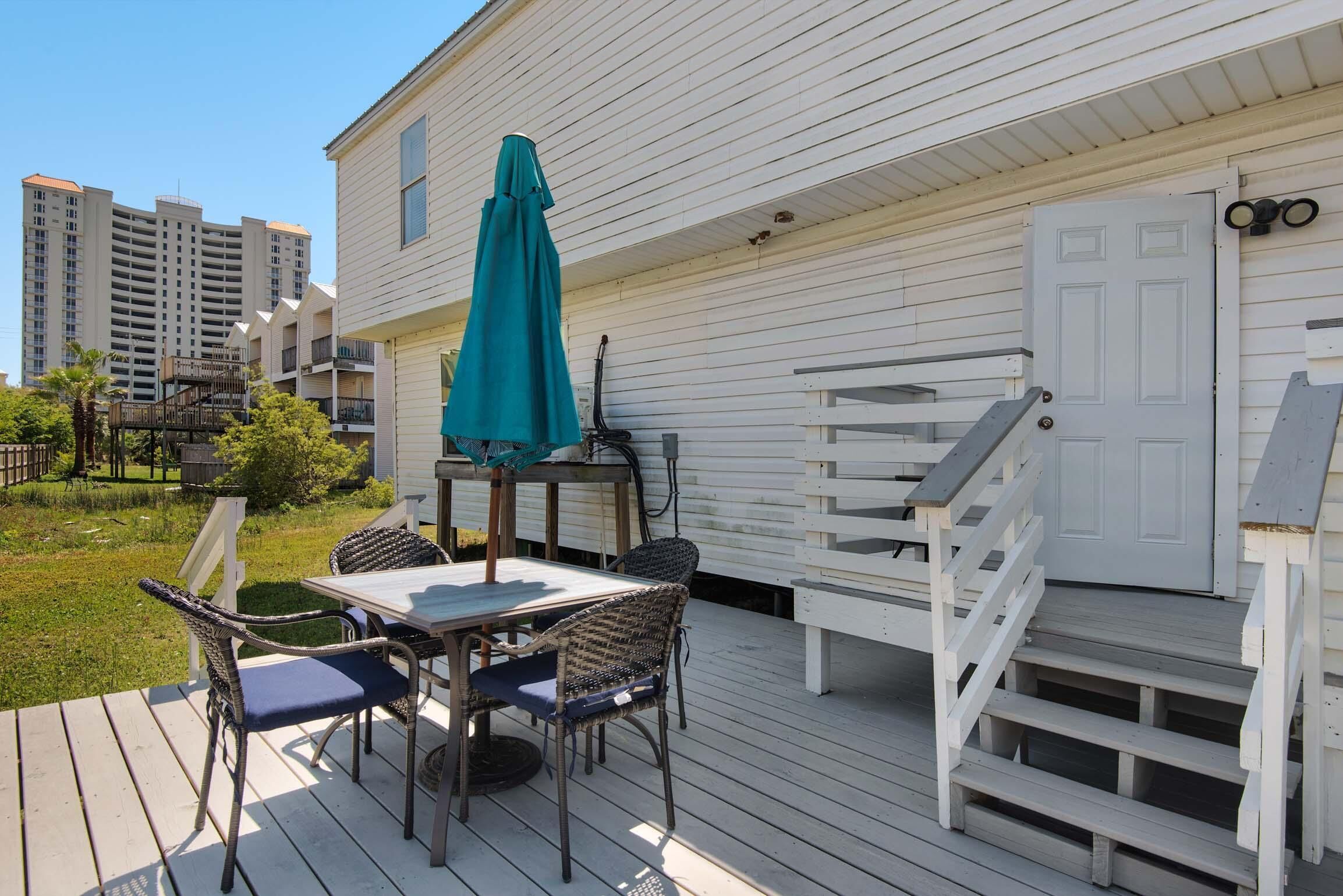 Une terrasse avec une table et des chaises, un parasol turquoise et un escalier menant à une porte.