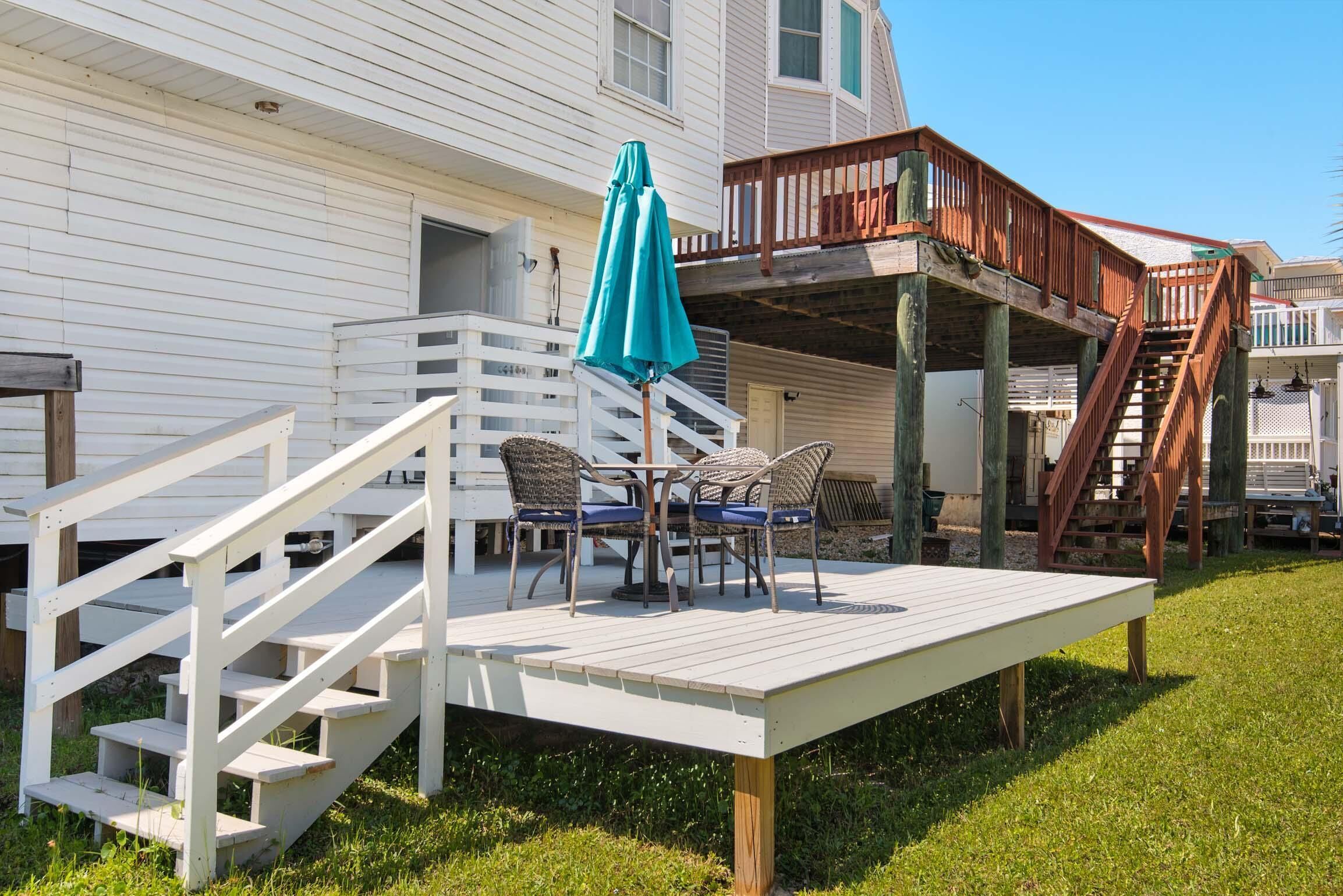 A wooden deck with a table and chairs, a blue umbrella, and a staircase leading to a balcony.