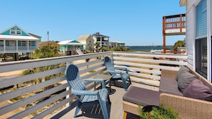 Une terrasse avec des sièges extérieurs, une vue sur la plage et un bâtiment doté d’un balcon.