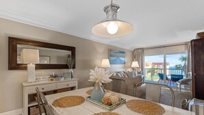 A dining area with a large table, placemats, a vase with flowers, and a view of the outdoors. - Point East 314 (New Smyrna Beach)