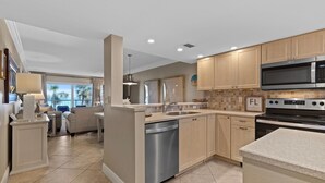A modern kitchen with wooden cabinets, a stainless steel dishwasher, a microwave, and a stove. - Point East 314 (New Smyrna Beach)
