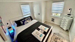 Ein Schlafzimmer mit Bett, Nachttischen, einem Schminktisch und Fenstern mit Jalousien.