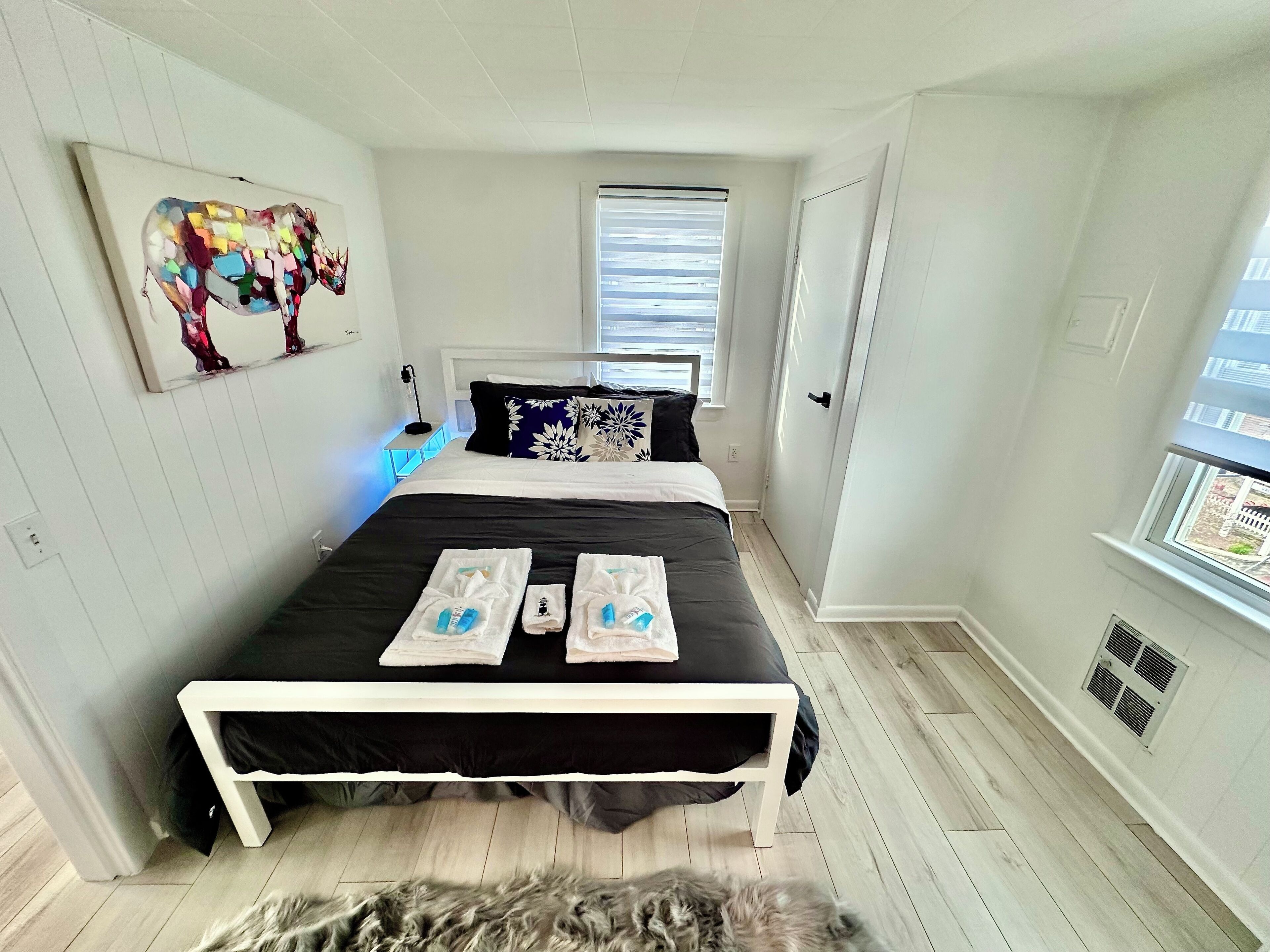 A bedroom with a bed, a window, a door, and a wall-mounted artwork.