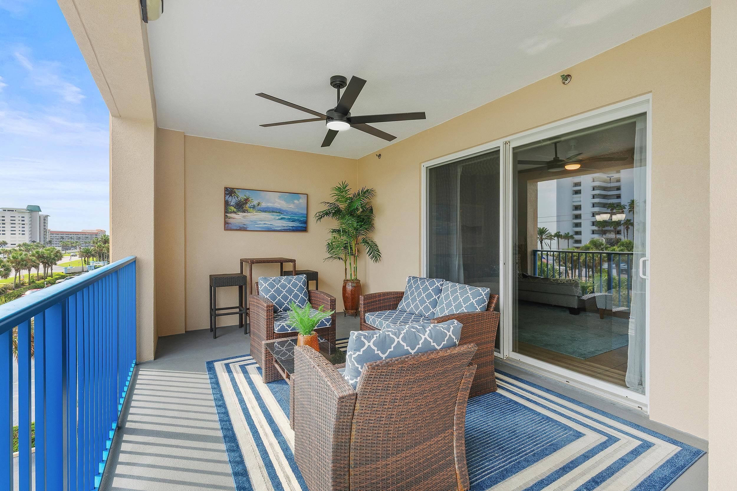 A balcony with wicker furniture, a ceiling fan, a painting, and a view of the cityscape.