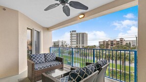 A balcony with wicker furniture, a ceiling fan, and a view of buildings and greenery.