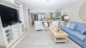 A living room with a TV, two striped armchairs, a blue sofa, a wooden coffee table, and a kitchen in the background. - Oceanwalk 16-602 (New Smyrna Beach)