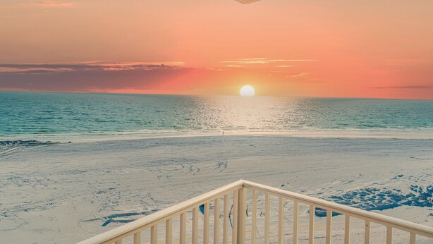 Vista de una playa al atardecer, con arena y una barandilla de madera al frente.