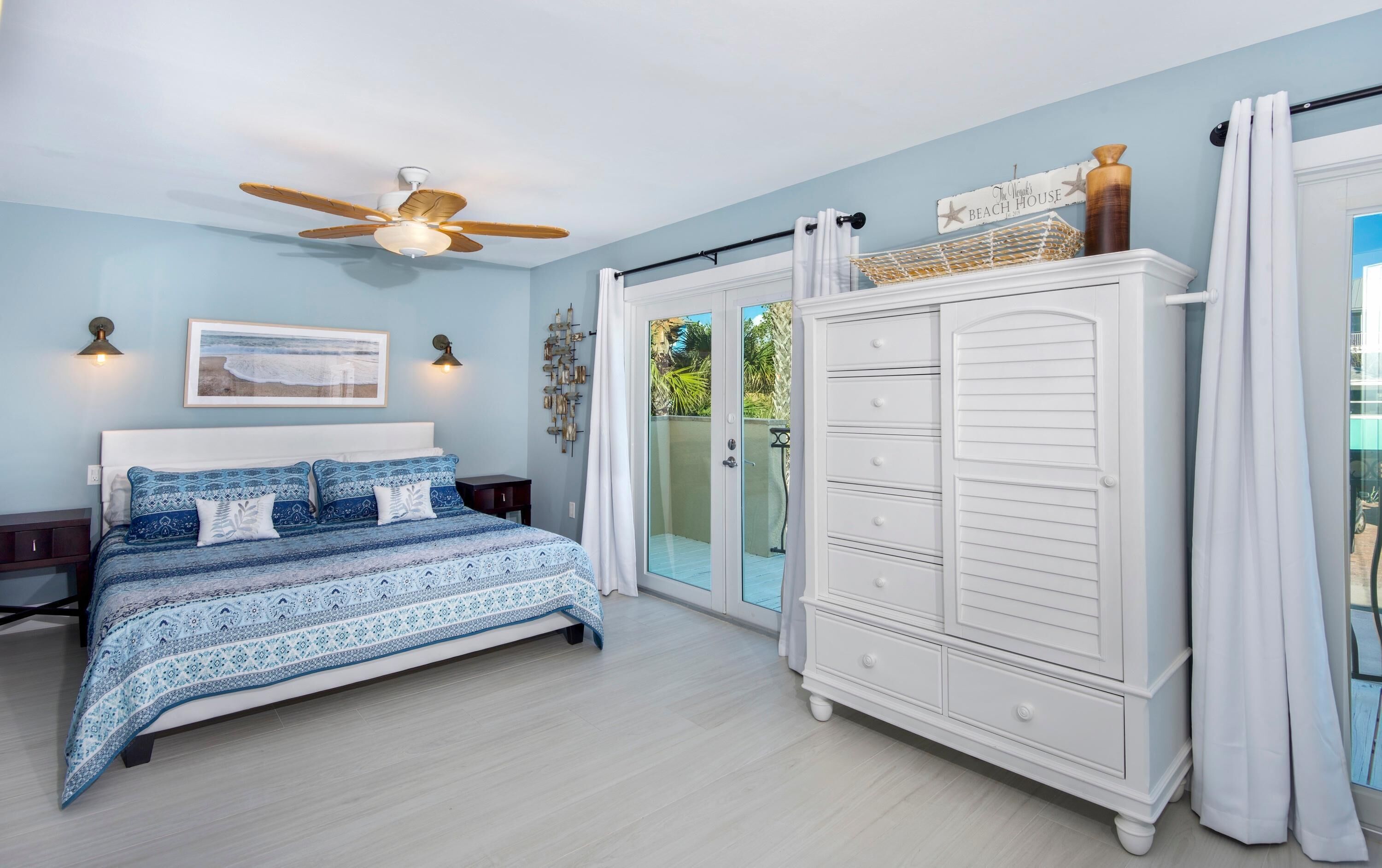 Quarto com cama, guarda-roupa, ventoinha no teto e vista para o exterior.