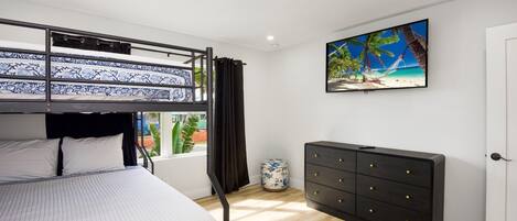 A room with a bunk bed, a dresser, a ceiling fan, a TV, and a window with curtains.