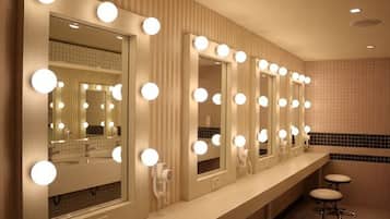 A bathroom with multiple mirrors, each surrounded by lights, and a vanity counter with stools.